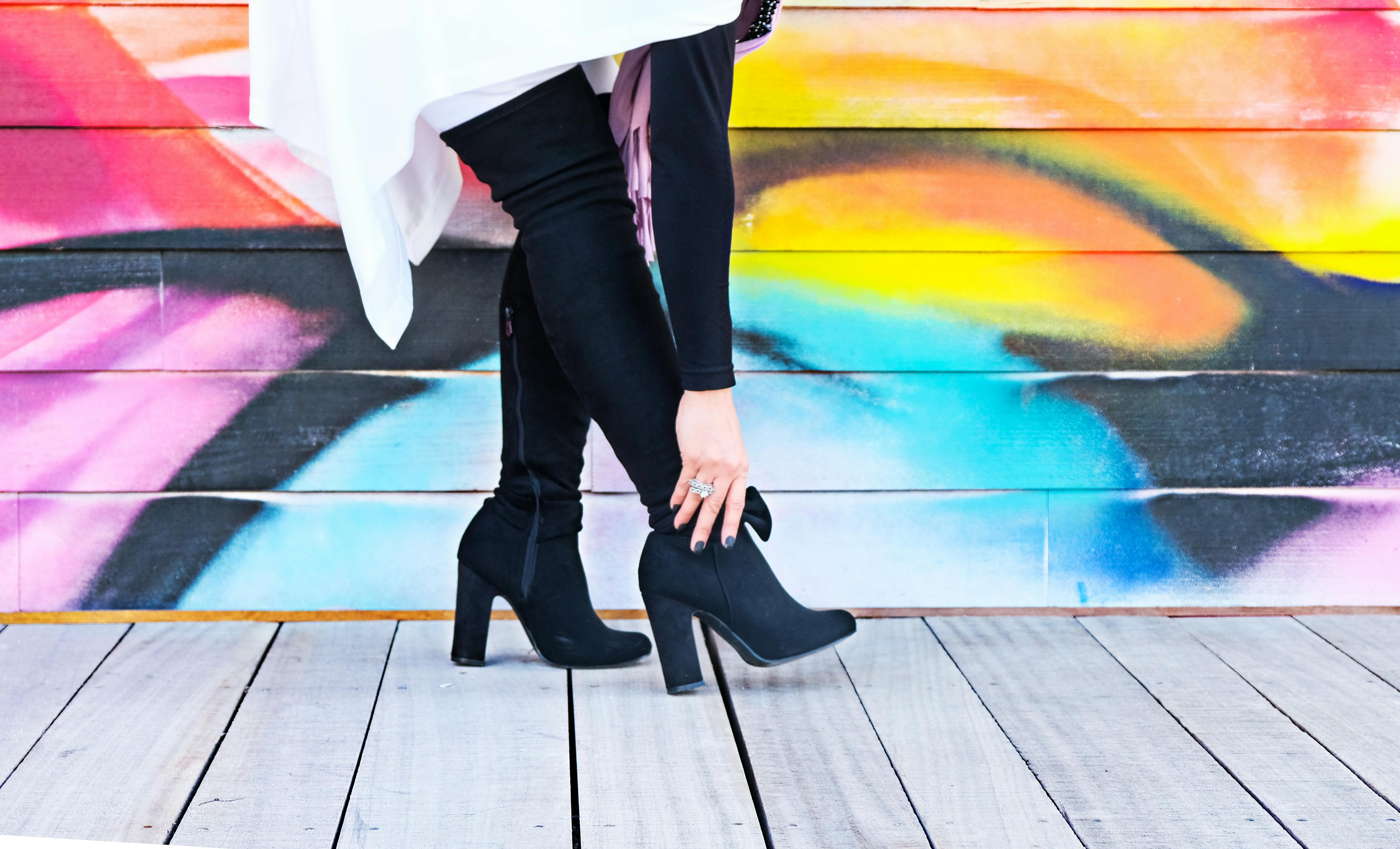 photo of woman touching right heeled shoe beside wall