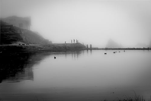 Grayscale Photo of Body of Water Near Mountain