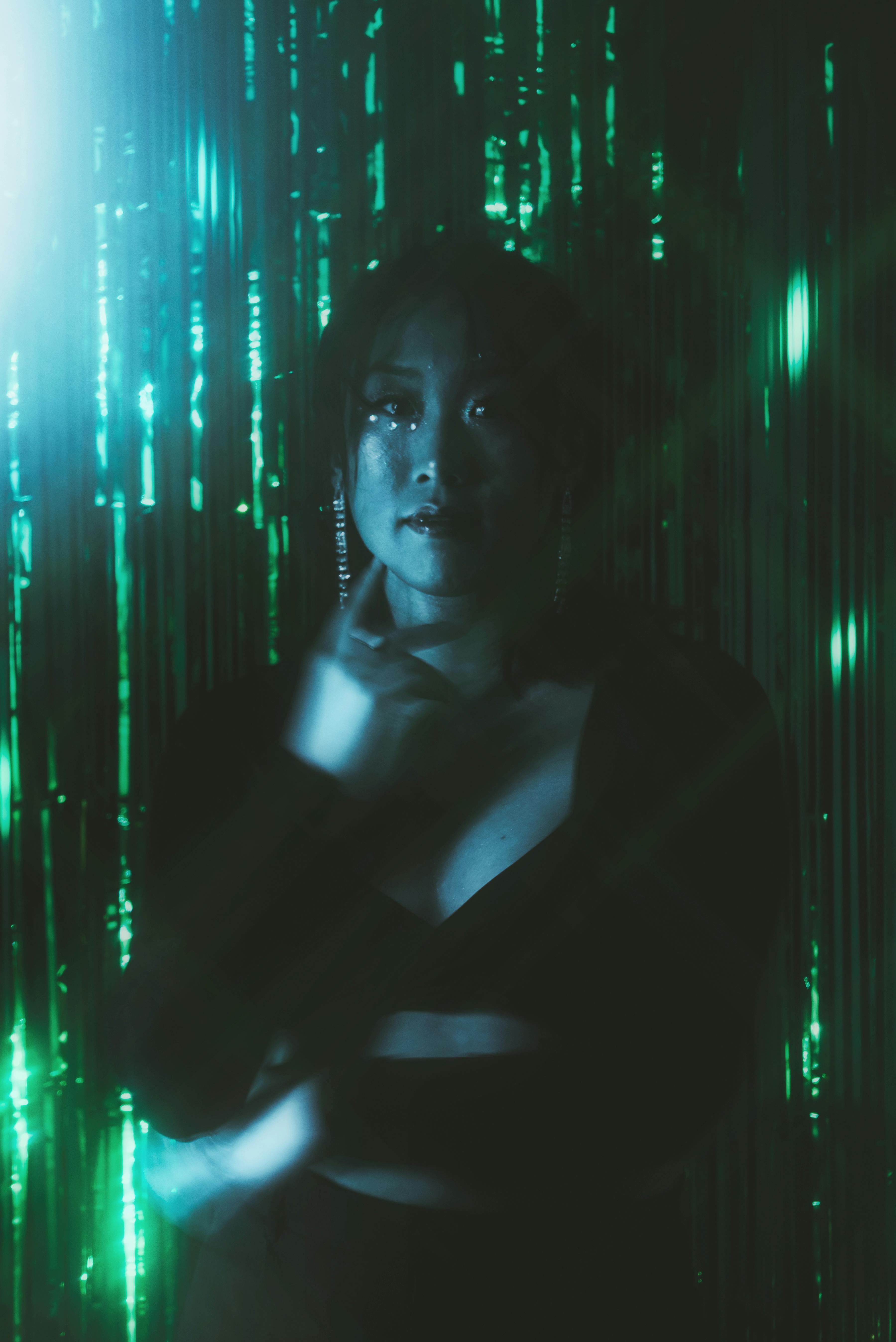 An artistic portrait of a woman in a moody, colorful lighting with sparkling tinsel backdrop.