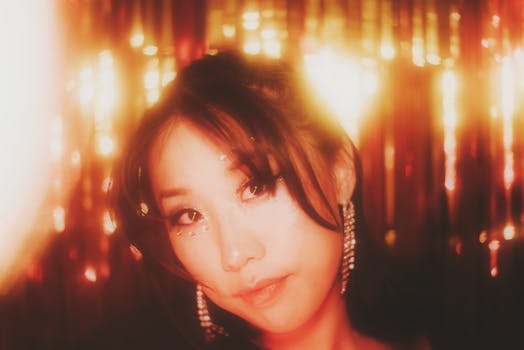 A dreamy portrait of a woman with sparkling makeup and glowing earrings, set against a warm, golden backdrop.