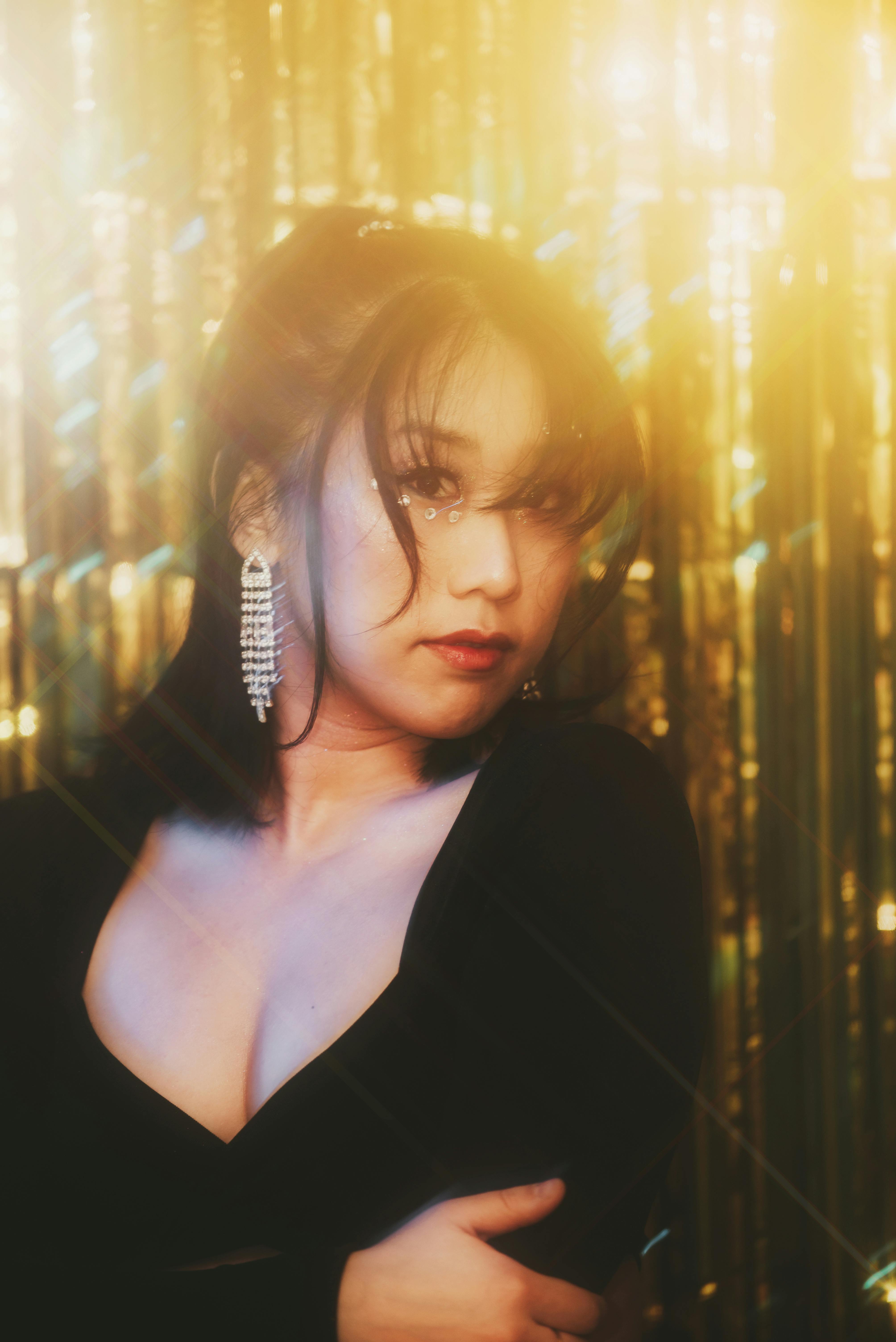 Elegant portrait of a woman with sparkling earrings and face jewels against a golden backdrop, exuding warmth and glamour.