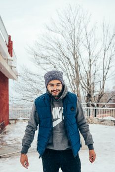 Cheerful young man in a beanie and vest enjoying a snowy winter day outdoors.