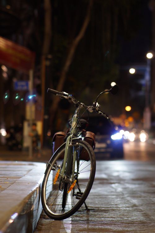 Free A bicycle parked on a city street at night with blurred car headlights in the background. Stock Photo