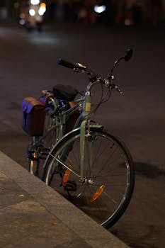 A classic bicycle with a brown saddlebag parked on an empty street at night.