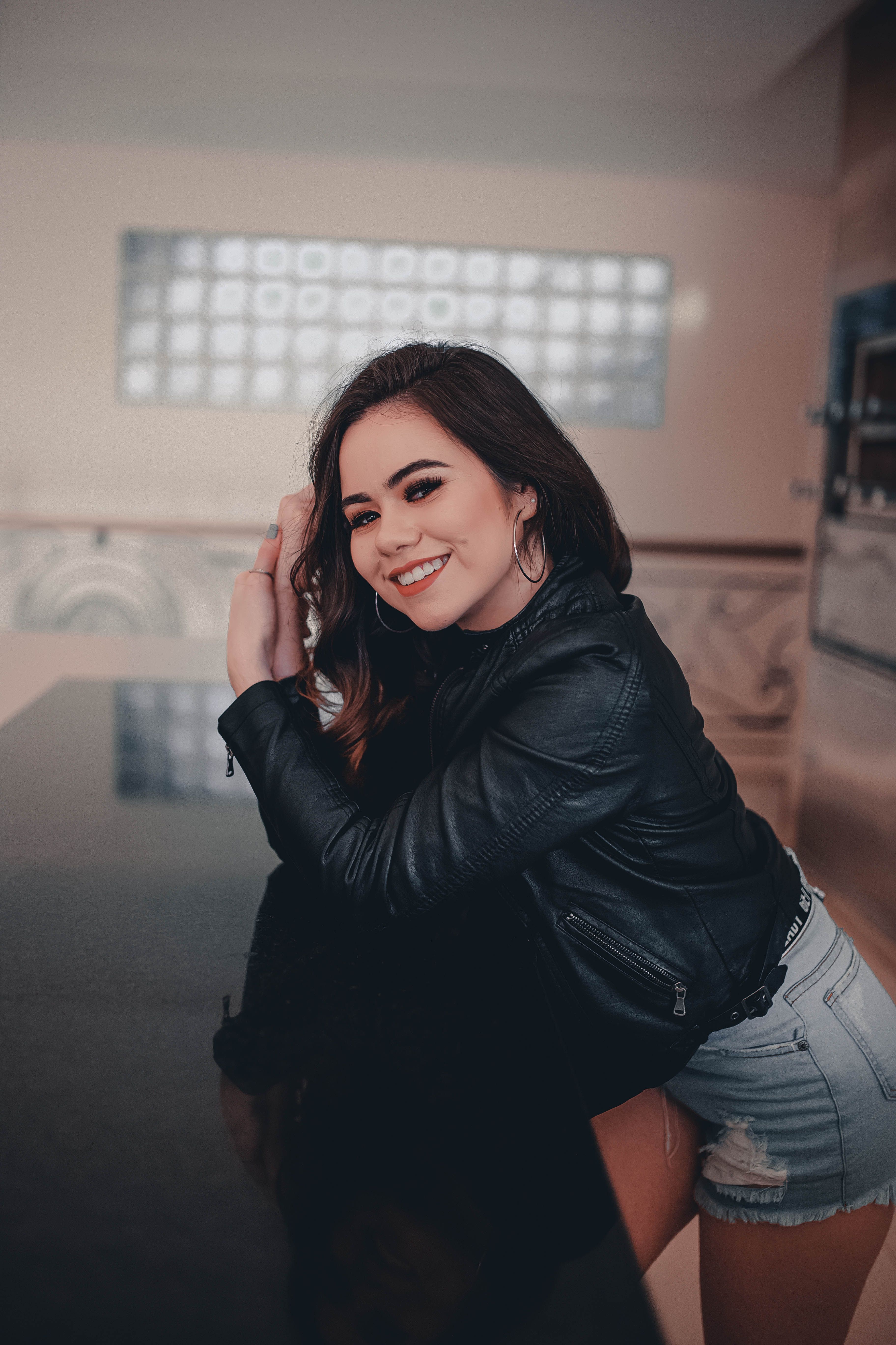 A Woman in Black Leather Jacket and Denim Shorts Smiling while Standing ...
