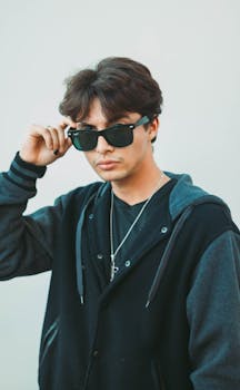 Young man with sunglasses and necklace posing confidently, showcasing modern fashion style.