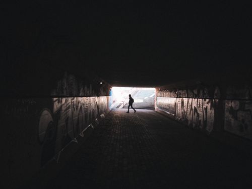 Free A lone person silhouetted walking through a graffiti-covered urban tunnel. Stock Photo