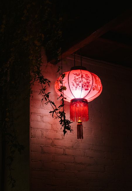 Brightly lit Chinese lantern hanging on a white brick wall, casting warm light.