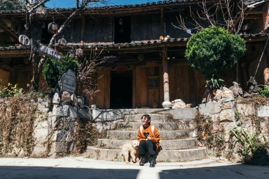 A woman sitting on stone steps with her dog at a rustic wooden homestay entrance.