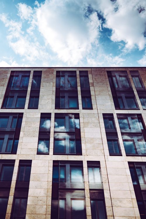 Free Modern office building in Frankfurt with glass windows reflecting clouds against a blue sky. Stock Photo
