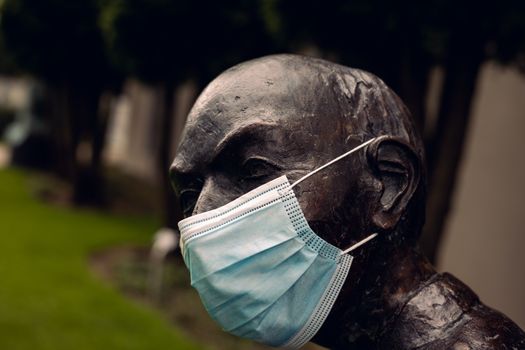 Close-up of a bronze statue outdoors with a face mask, symbolizing pandemic precautions.