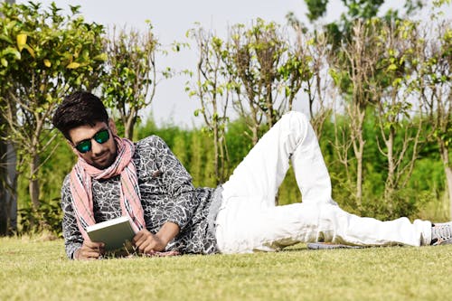 Man in White Pants Wearing Sunglasses Reading Book