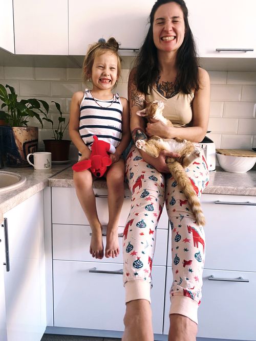 Free A happy mother and daughter sit on a kitchen counter with their cat, showcasing family joy. Stock Photo