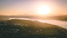 从空中俯瞰，风景如画的日落映照在一条河流上，周围是郁郁葱葱的绿色和分散的房屋