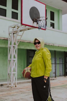 Outdoor portrait of a woman with a basketball, in a hijab and neon jacket.