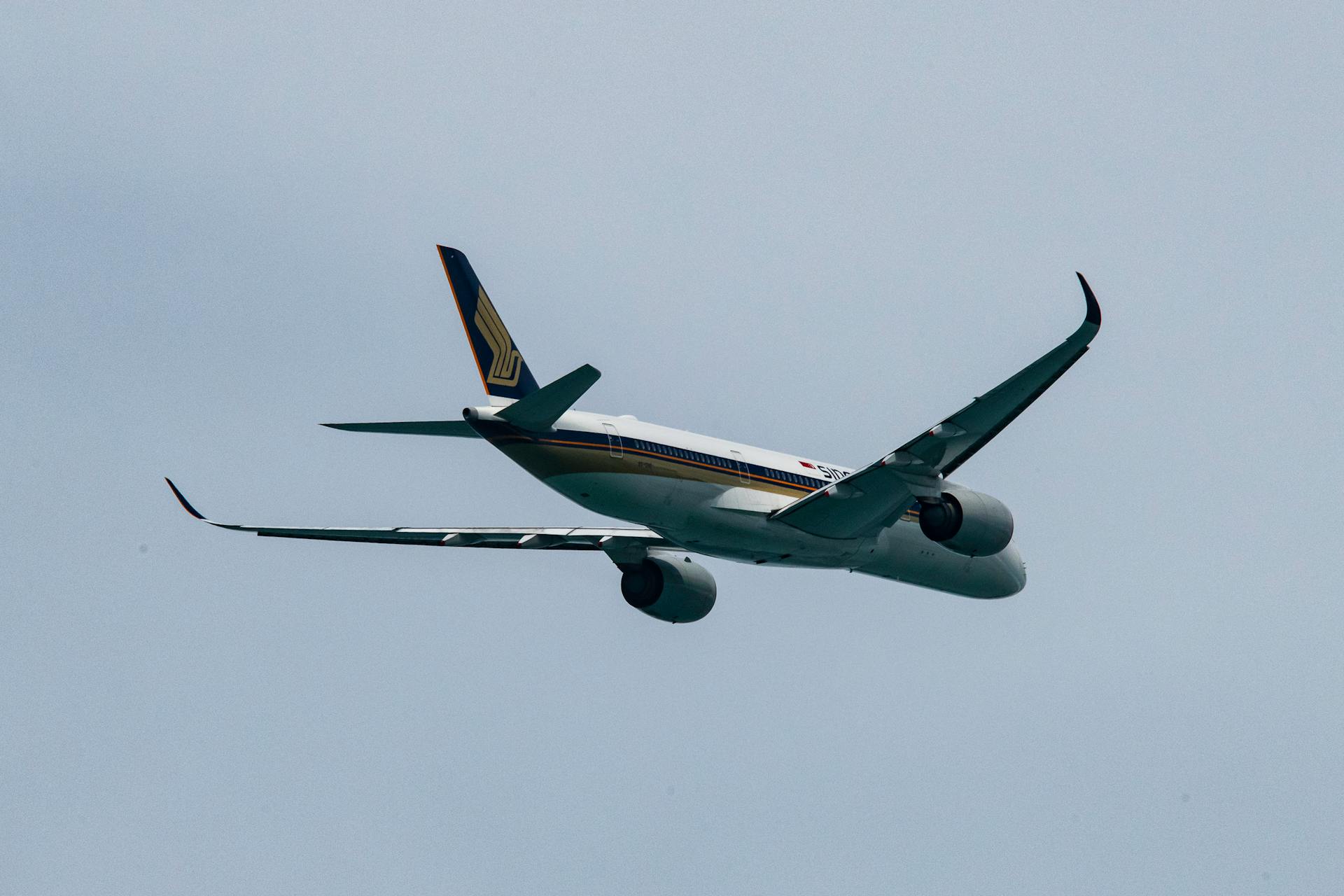 Singapore Airlines airplane flying against a clear blue sky, viewed from below.