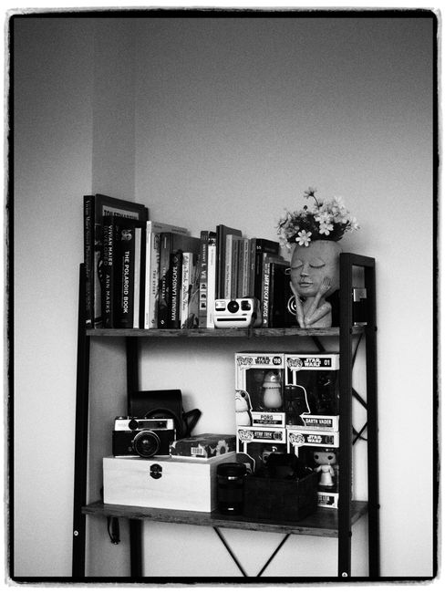 Monochrome image of a bookshelf with books, vintage cameras, and collectibles.
