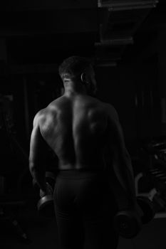 Monochrome image of a muscular man holding dumbbells in a gym, showcasing strength and fitness.