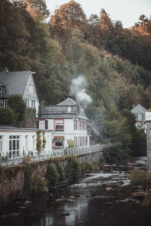 Free Scenic view of charming riverside houses in Monschau, Germany with chimney smoke rising. Stock Photo