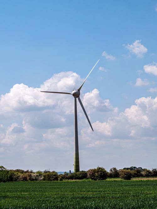 Free A tall wind turbine stands in a lush green field under a bright blue sky with fluffy clouds. Stock Photo