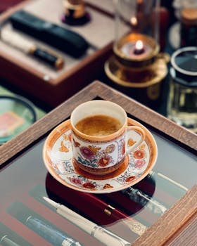 Artisan coffee displayed in a vintage floral cup with luxury pens and accessories.
