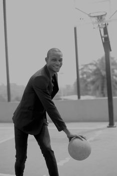 African American man in a suit playing basketball outdoors, smiling.