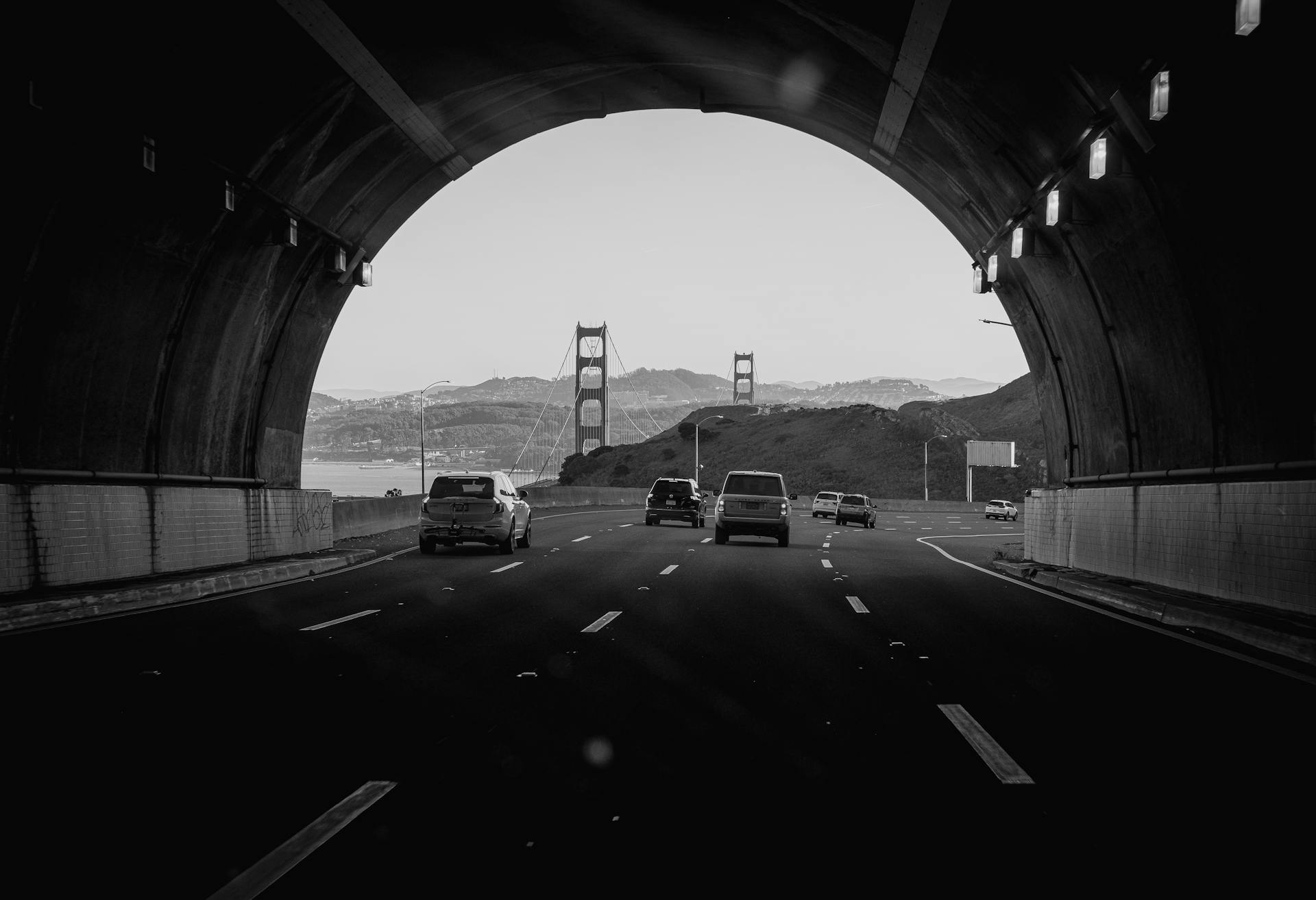 Monochrome view from tunnel framing the Golden Gate Bridge with moving vehicles.