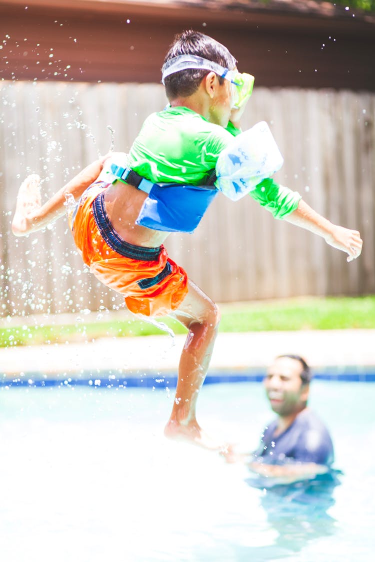 Boy In Green Crew-neck Shirt And Orange Shorts Jump Over Swimming Pool