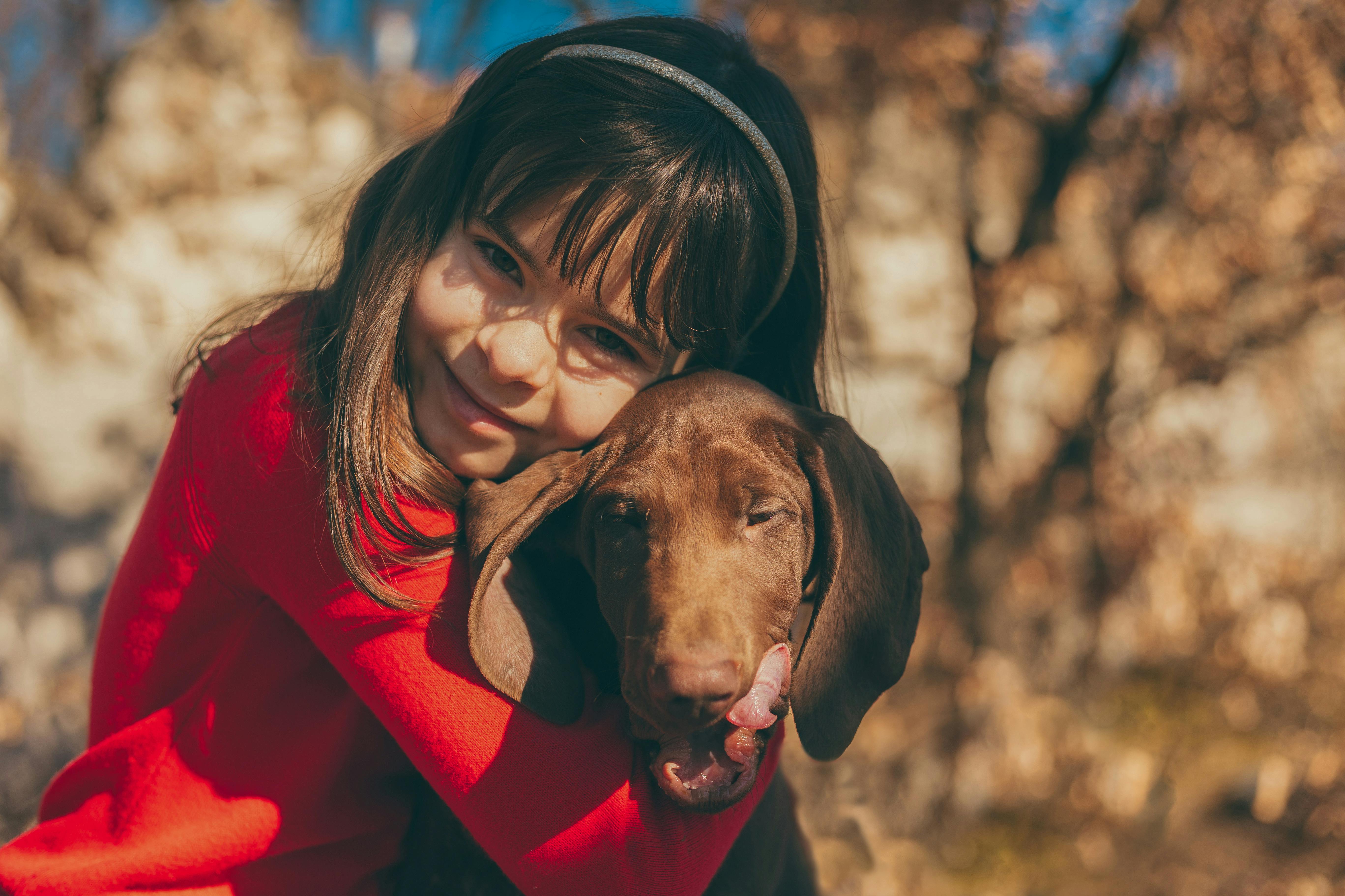 a young girl in red long sleeves embracing her dog