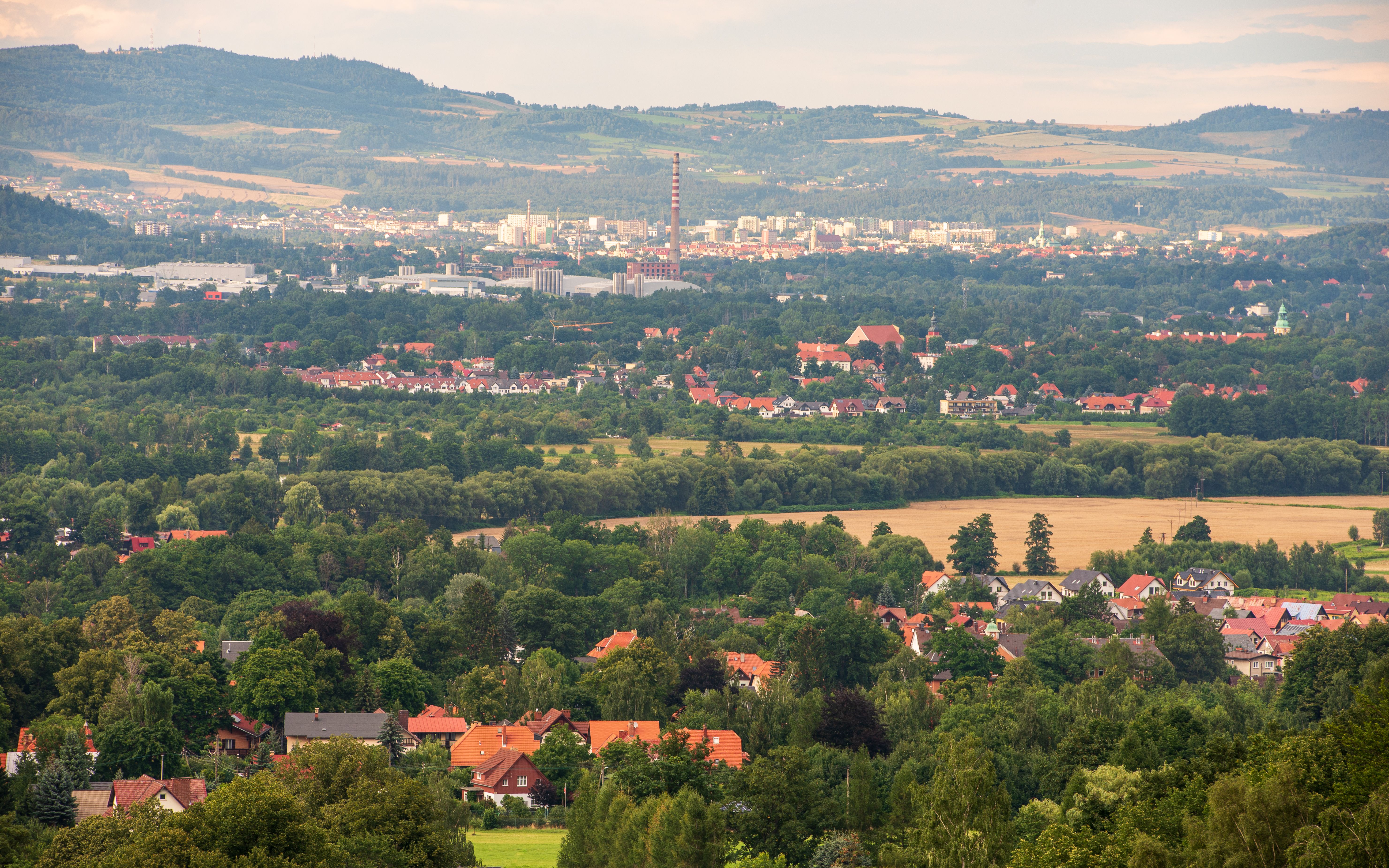Aerial view of a sprawling cityscape surrounded by vibrant green fields and forests.