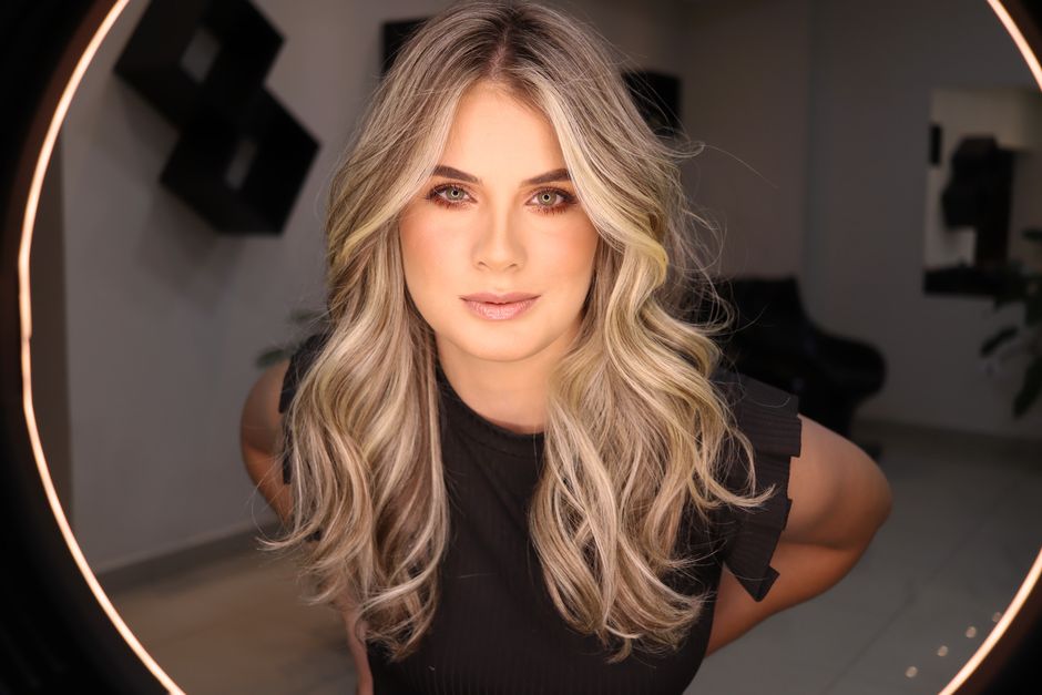 Close-up portrait of a blonde woman with stylish makeup and elegant curls, looking confidently into the camera.