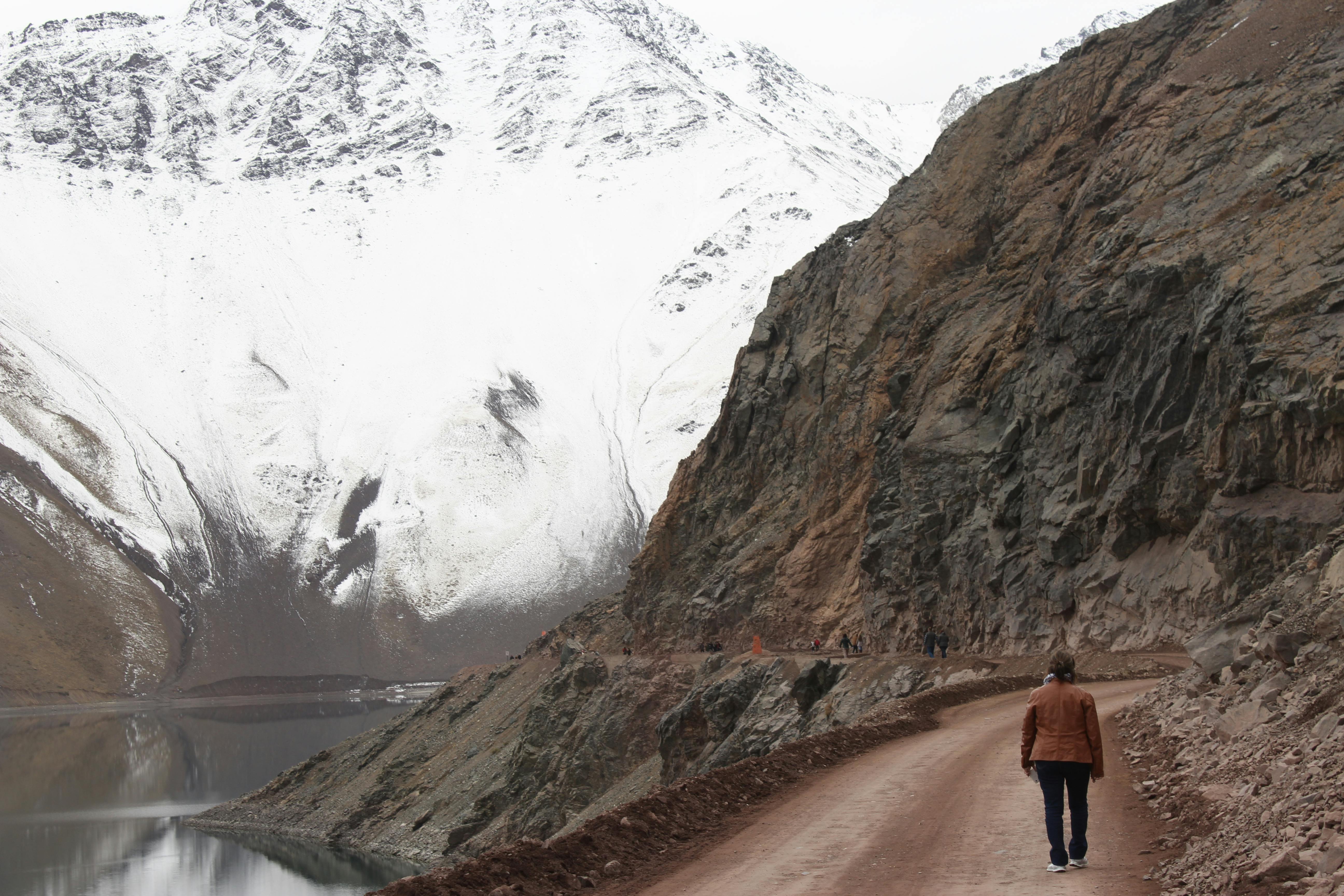 woman with brown jacket walking beside body of water