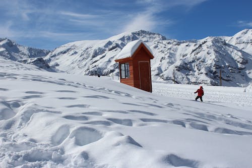 Foto De Uma Pessoa Com Casaco Vermelho Perto De Casa Marrom Na Neve