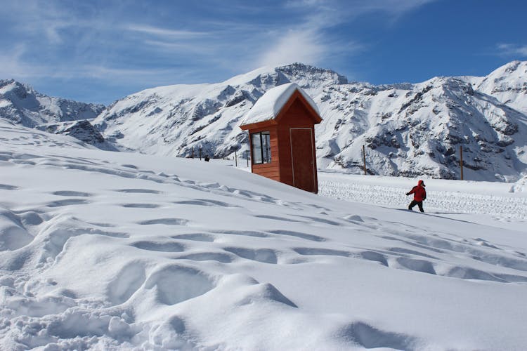 Photo Of Person In Red Coat Near Brown House In Snow