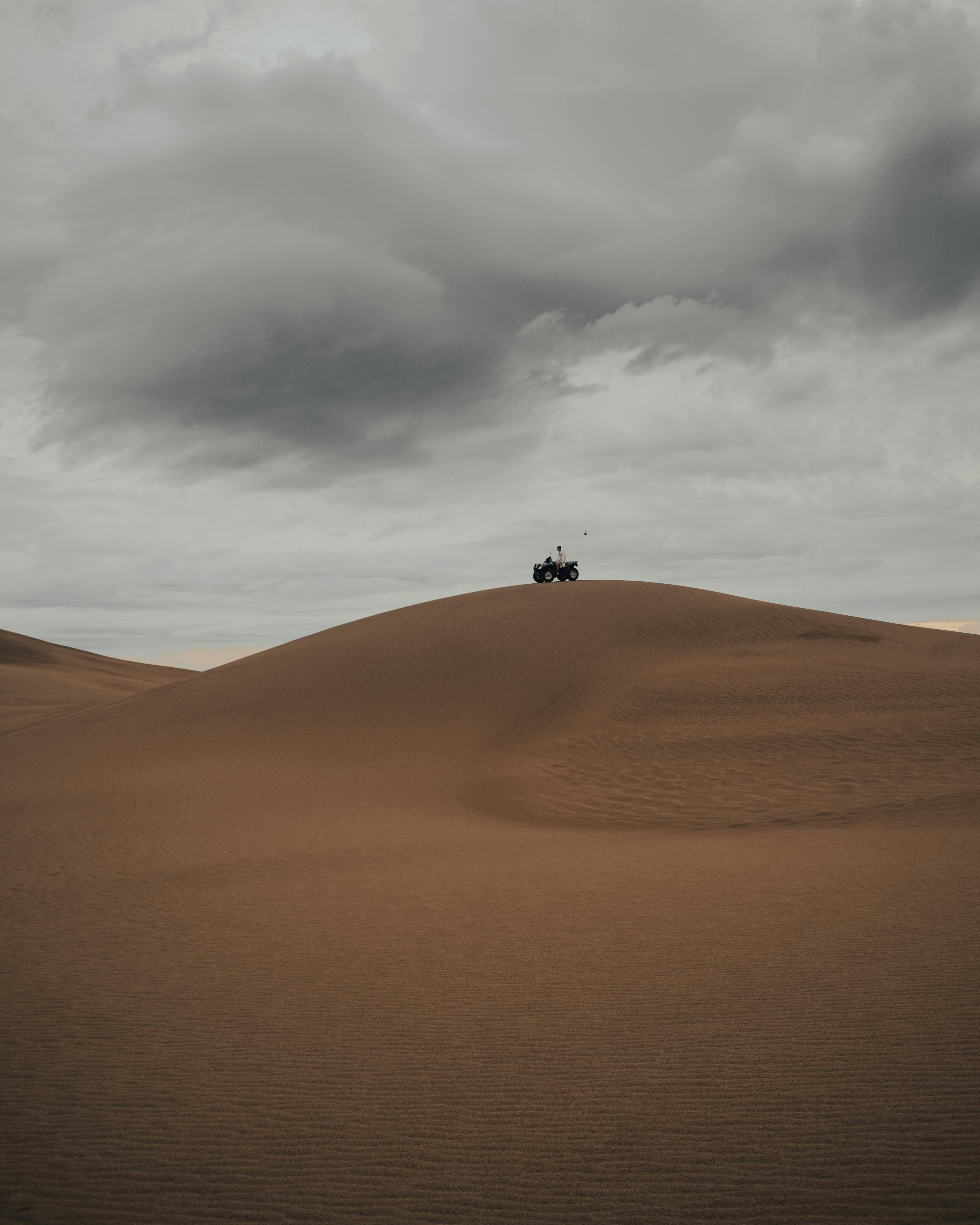 A solitary quad bike on a vast desert dune under an overcast sky, evoking adventure.