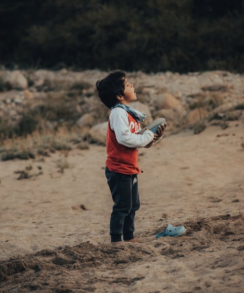 A Young Boy in Black Pants Standing on the Beach Sand