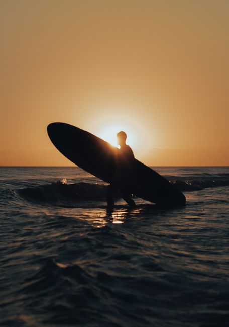A serene silhouette of a surfer carrying a board during a sunset beach scene.
