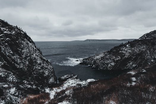 Majestic winter seascape featuring snow-dusted cliffs and a calm ocean under cloudy skies.