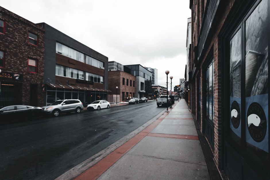 Moody urban street with parked cars and wet pavement after rain, showcasing modern architecture.