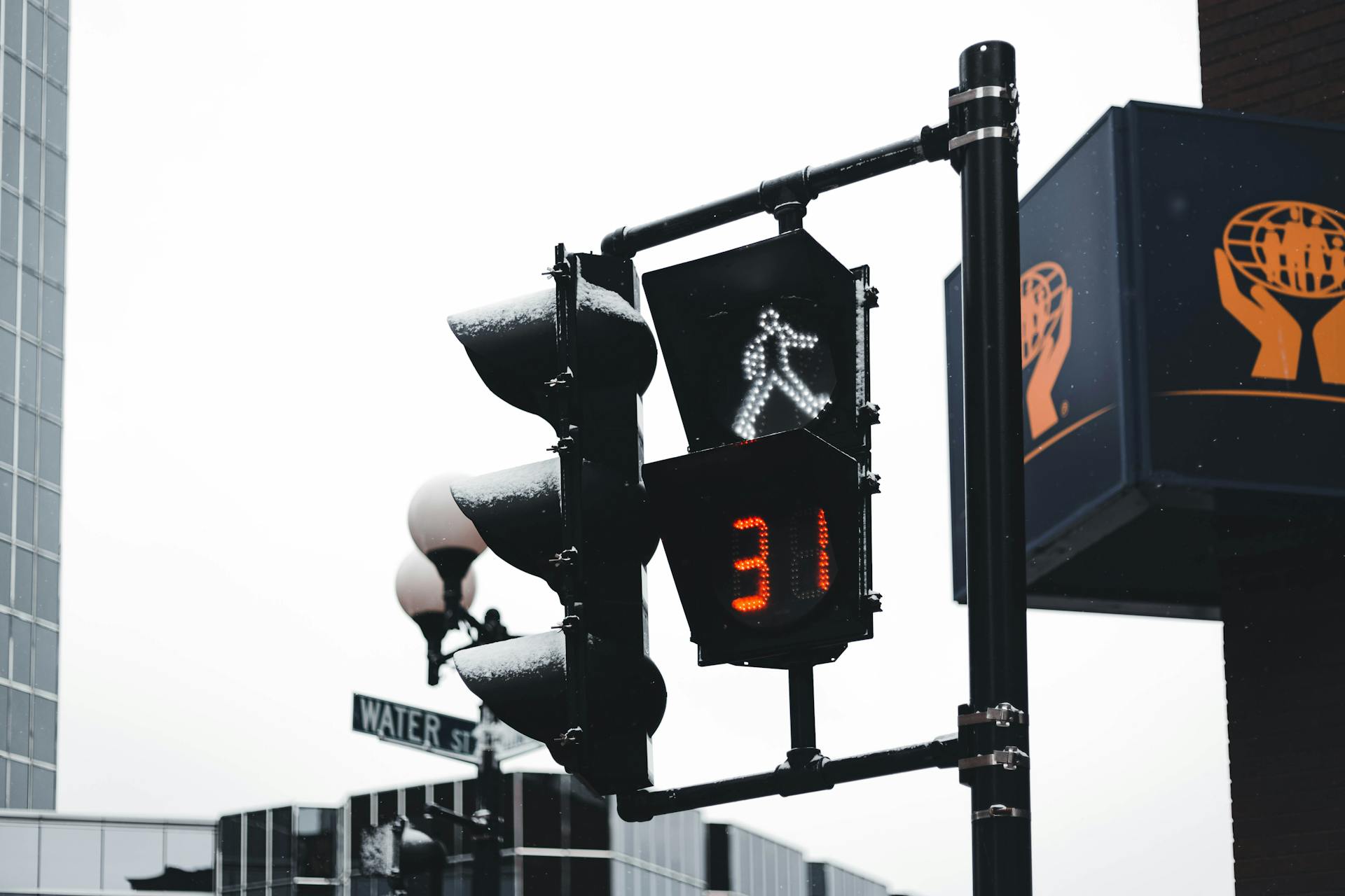 Close-up of a pedestrian traffic light at Water Street intersection, displaying a countdown timer on a cloudy day.