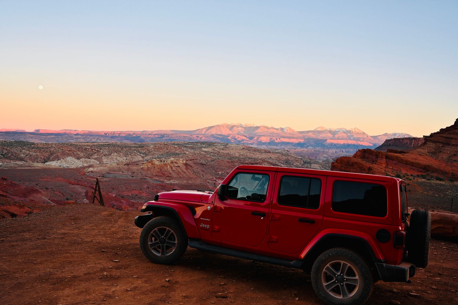 Red Jeep Wrangler parked on Utah desert overlanding route with red rock canyons and La Sal Mountains glowing at golden hour
