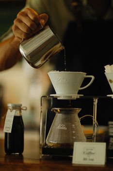 Close-up of hand pouring hot water for pour-over coffee brewing in a cafe setting.