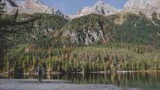 一位徒步旅行者站在宁静的山湖边，背景是郁郁葱葱的森林