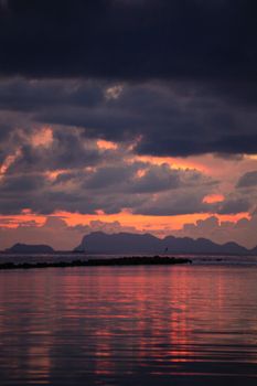 Capture of a vibrant sunset with dramatic clouds over a calm sea reflecting the pink and orange hues.