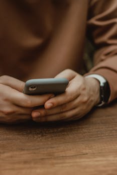 Close-up of hands using a smartphone on a wooden table in Istanbul, Turkey.