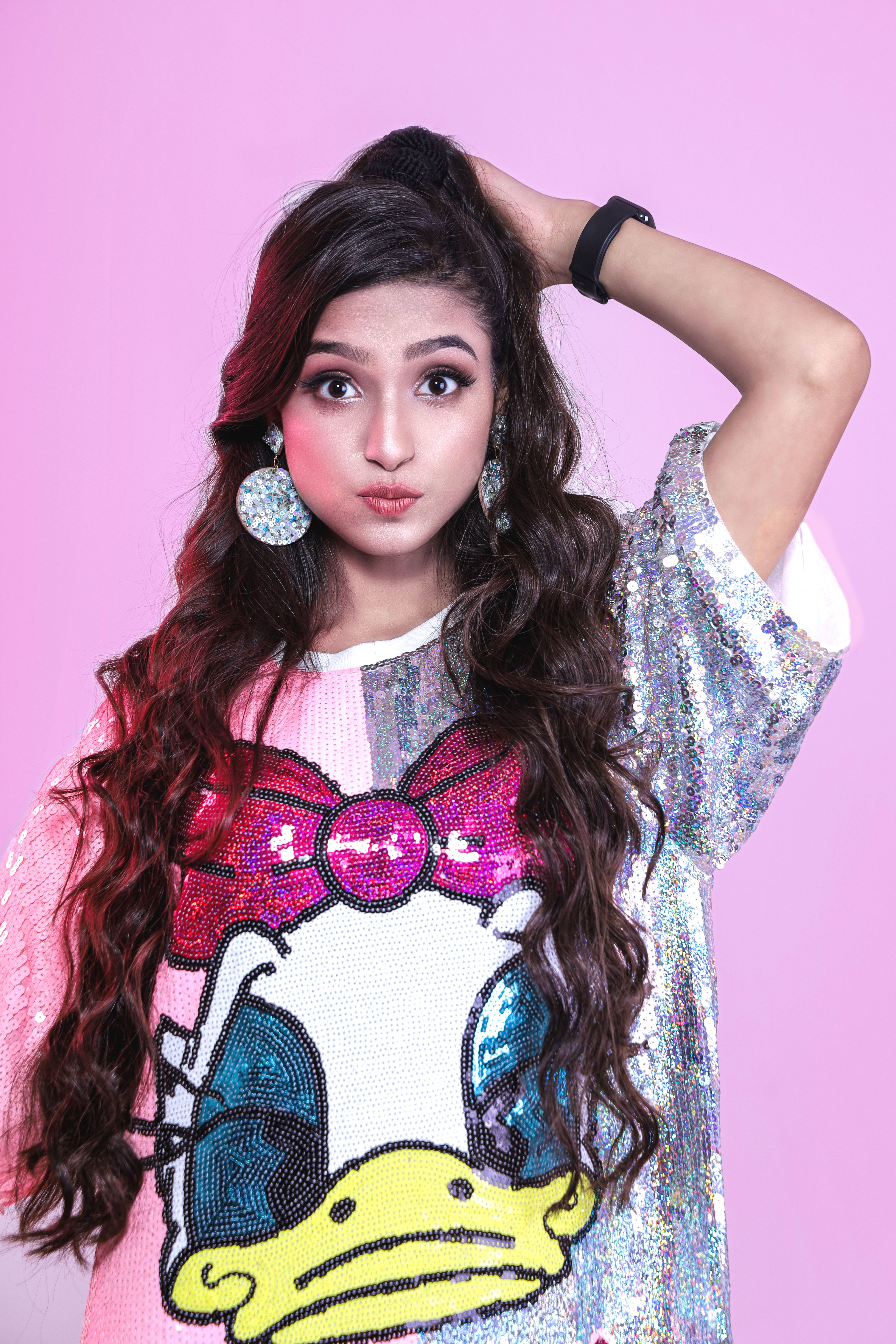 Fashionable young woman poses confidently in a sequined shirt with a cartoon print.