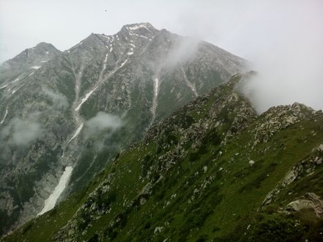 Foggy mountain peaks with green slopes and mist create a serene natural landscape view.