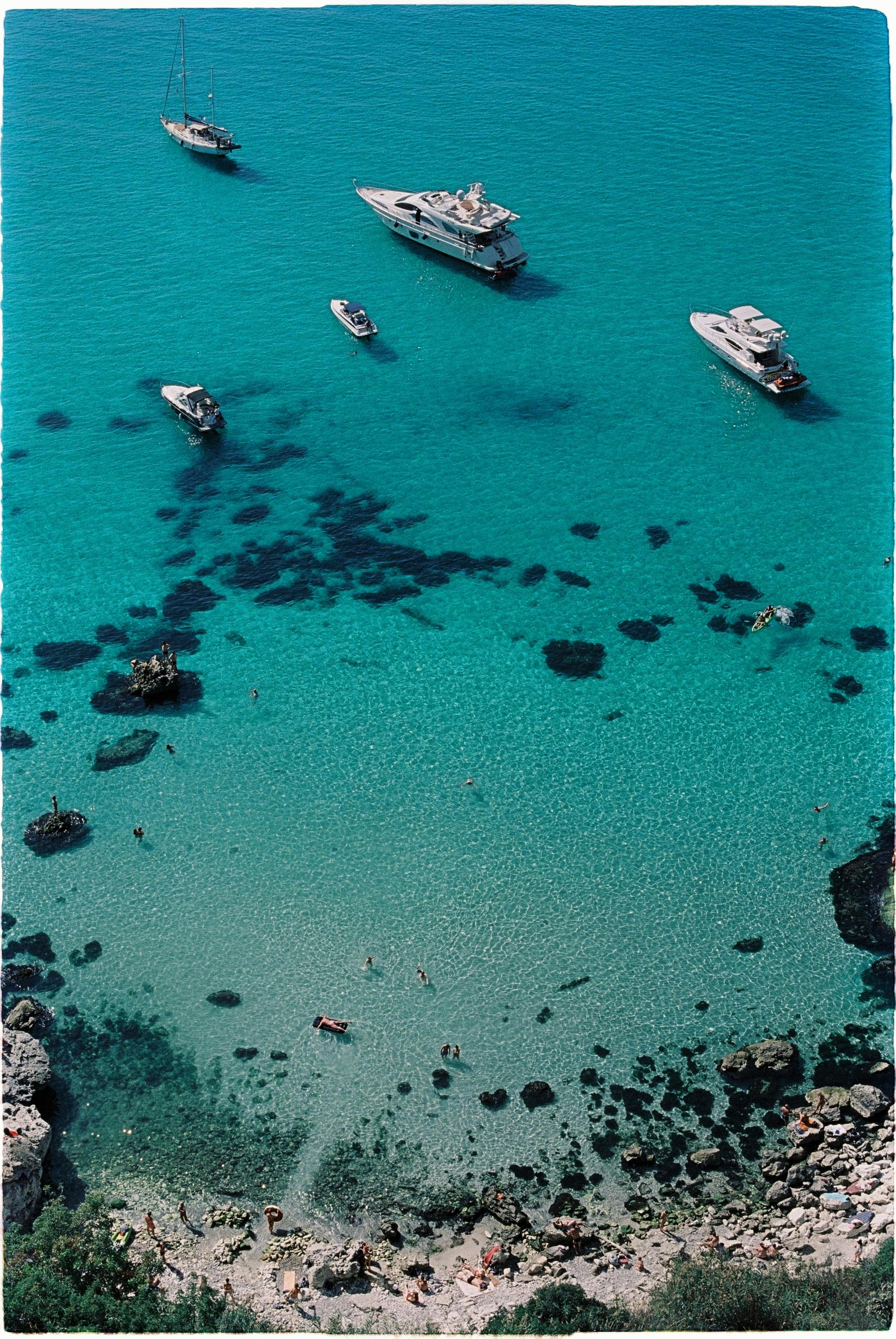 Stunning aerial view of a turquoise Mediterranean beach with yachts and clear waters.