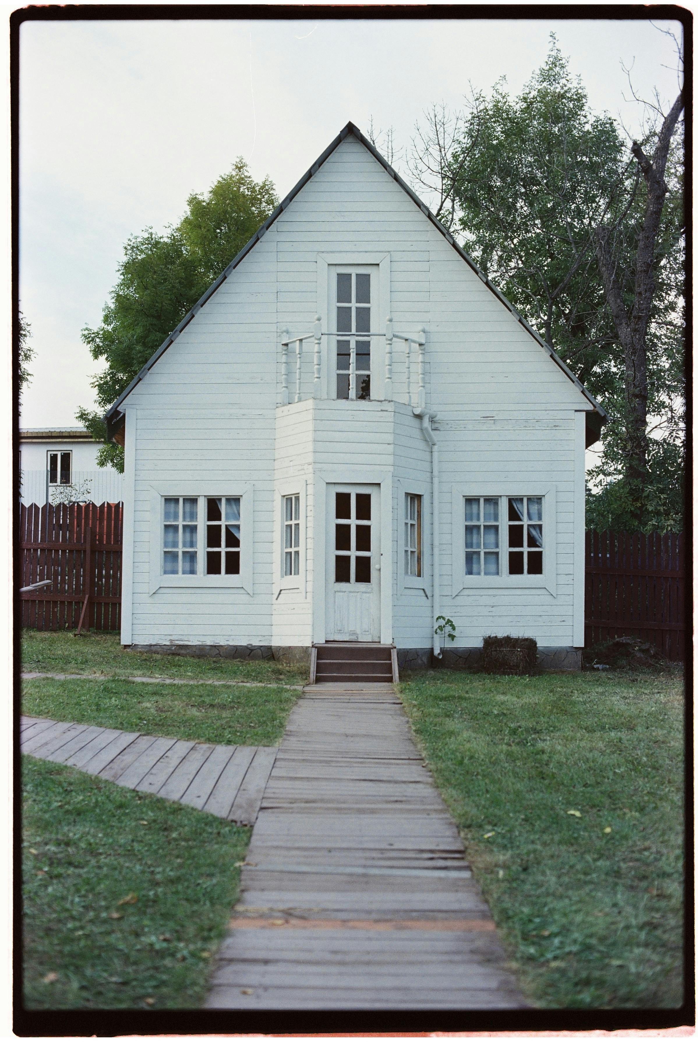 Quaint wooden house with a boardwalk leading to the entrance, surrounded by lush greenery.