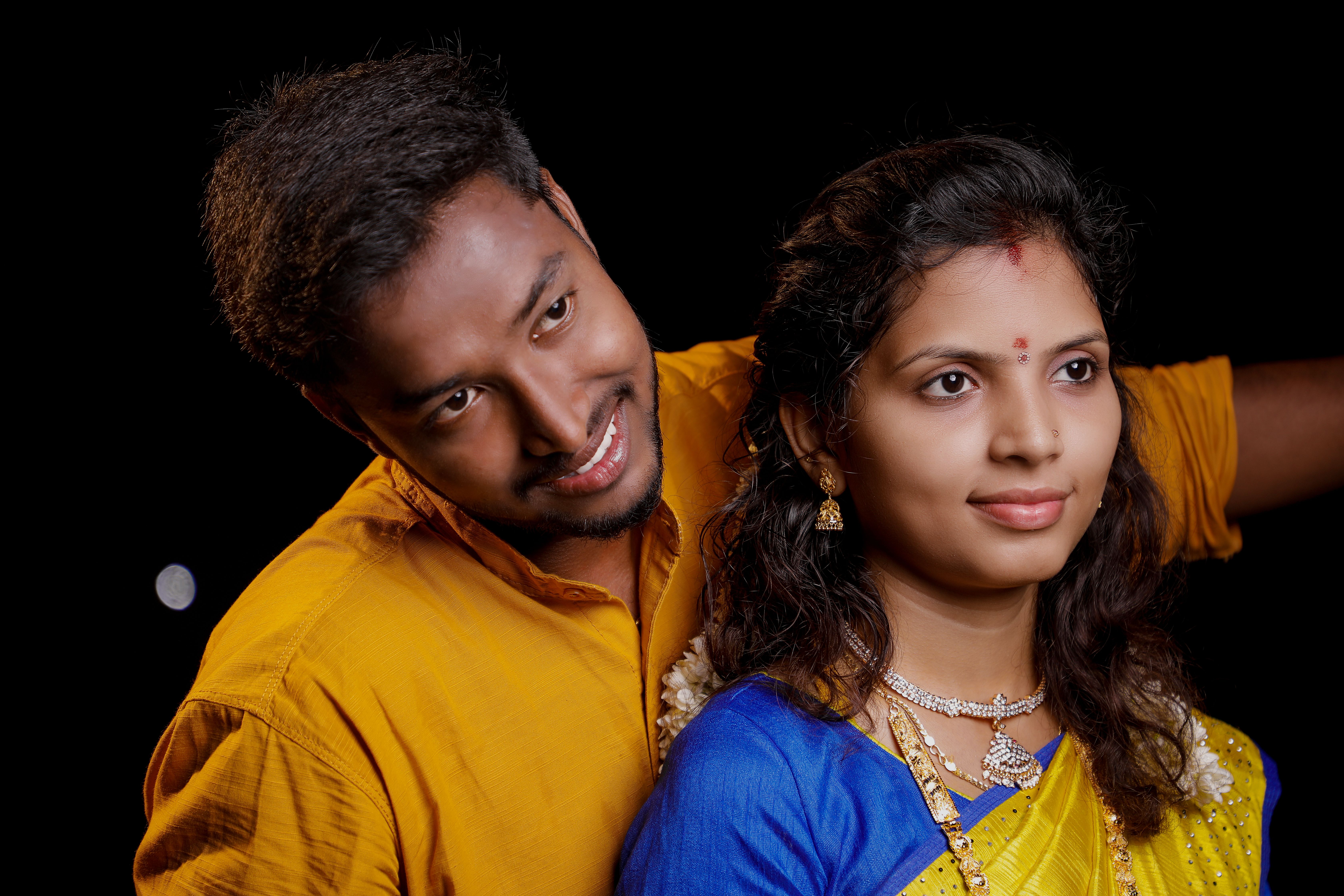Smiling Indian couple wearing traditional attire on a black background, embodying joy and tradition.